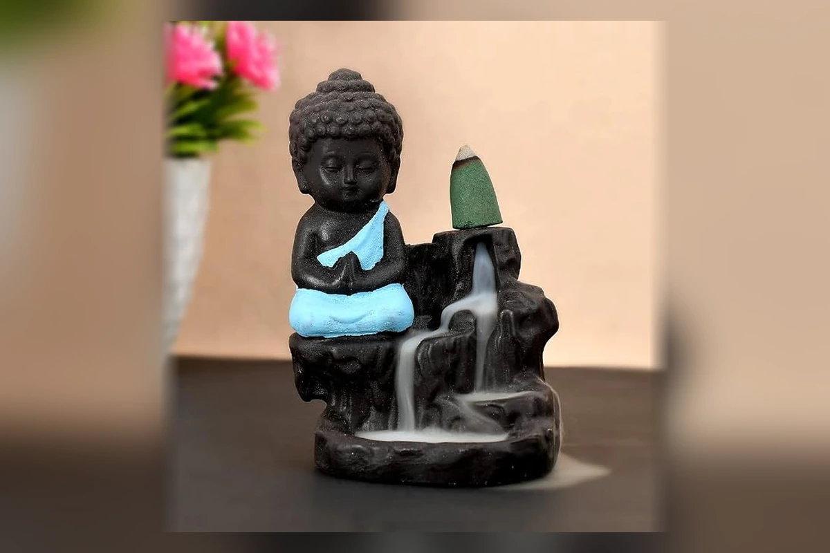 A dedicated meditating monk backflow incense burner creating a serene cascading smoke waterfall for morning meditation.
