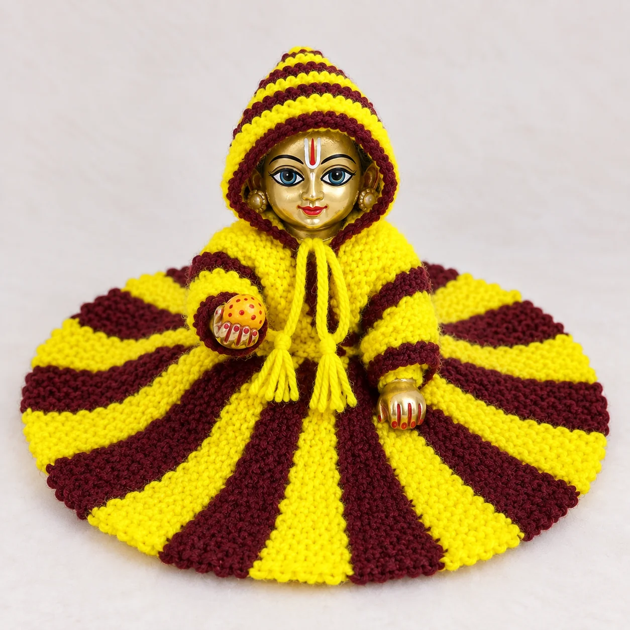 Laddu Gopal Ji wearing a handmade yellow and maroon striped woollen poshak with matching hood