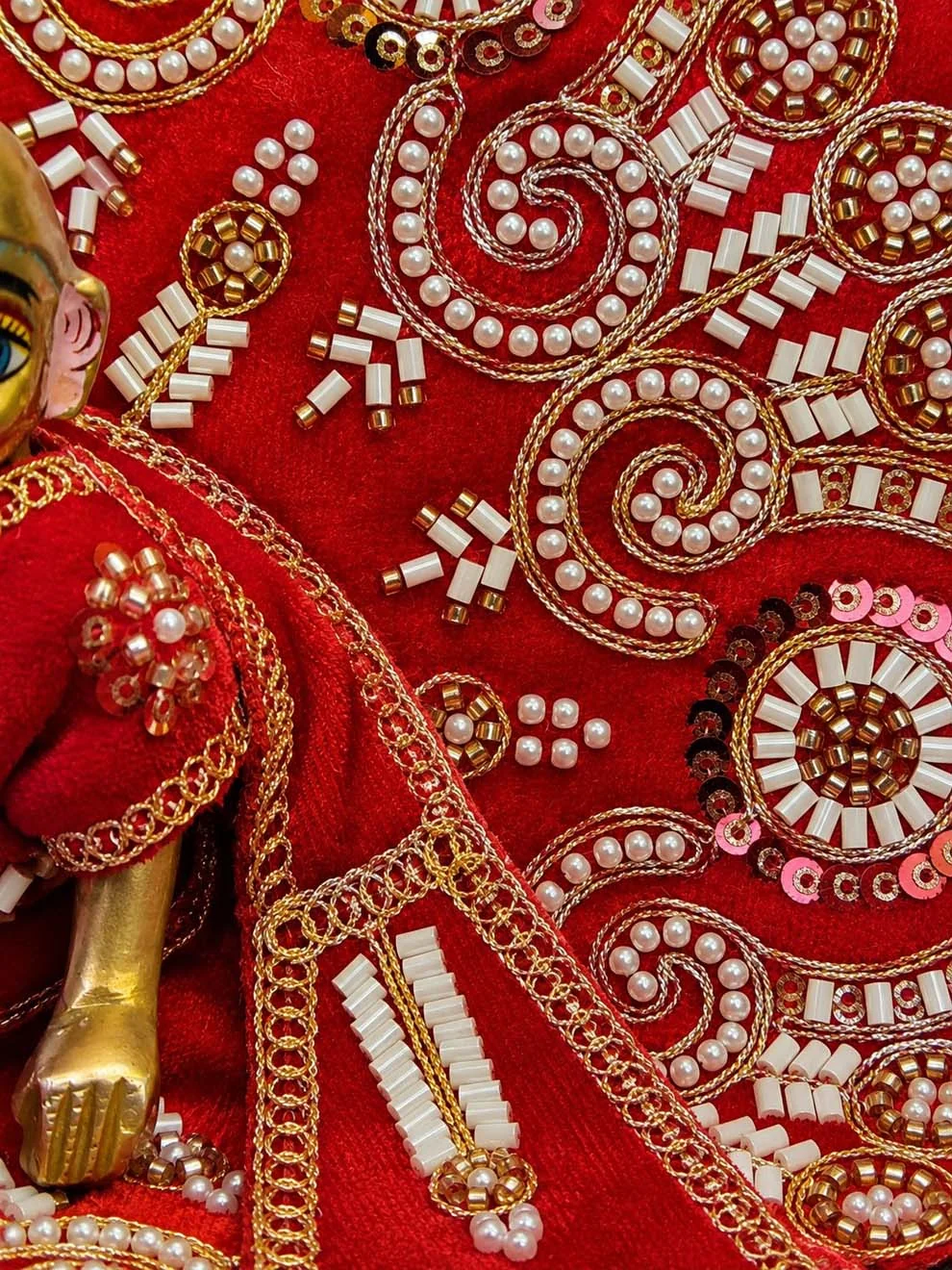 Close-up of hand-finished stone and pearl work on a red velvet OM Poshak dress for Laddu Gopal Ji